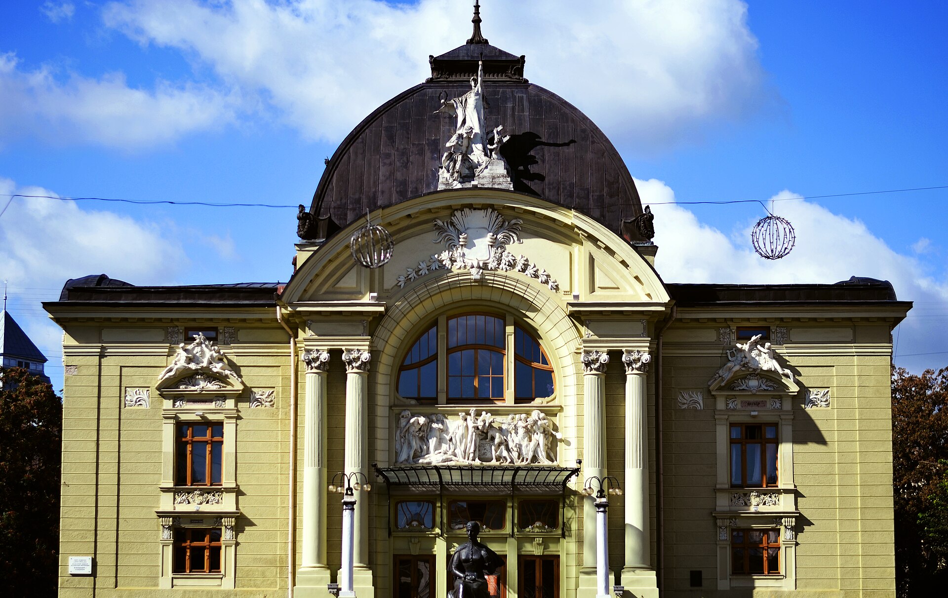 Головний фасад Чернівецького театру з великим арковим вікном, колонами, рельєфом над входом і скульптурою у верхній частині фасаду
