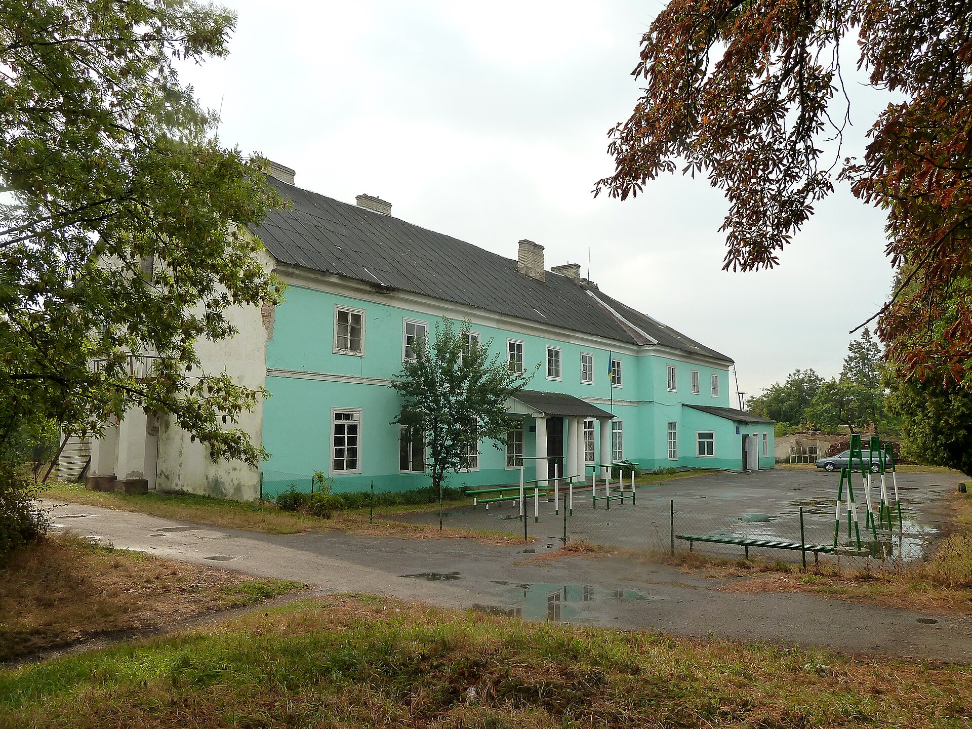 Збережений флігель палацу Браницьких у Любомлі: довга двоповерхова світло-зелена будівля зі скатним дахом і входом із колонами