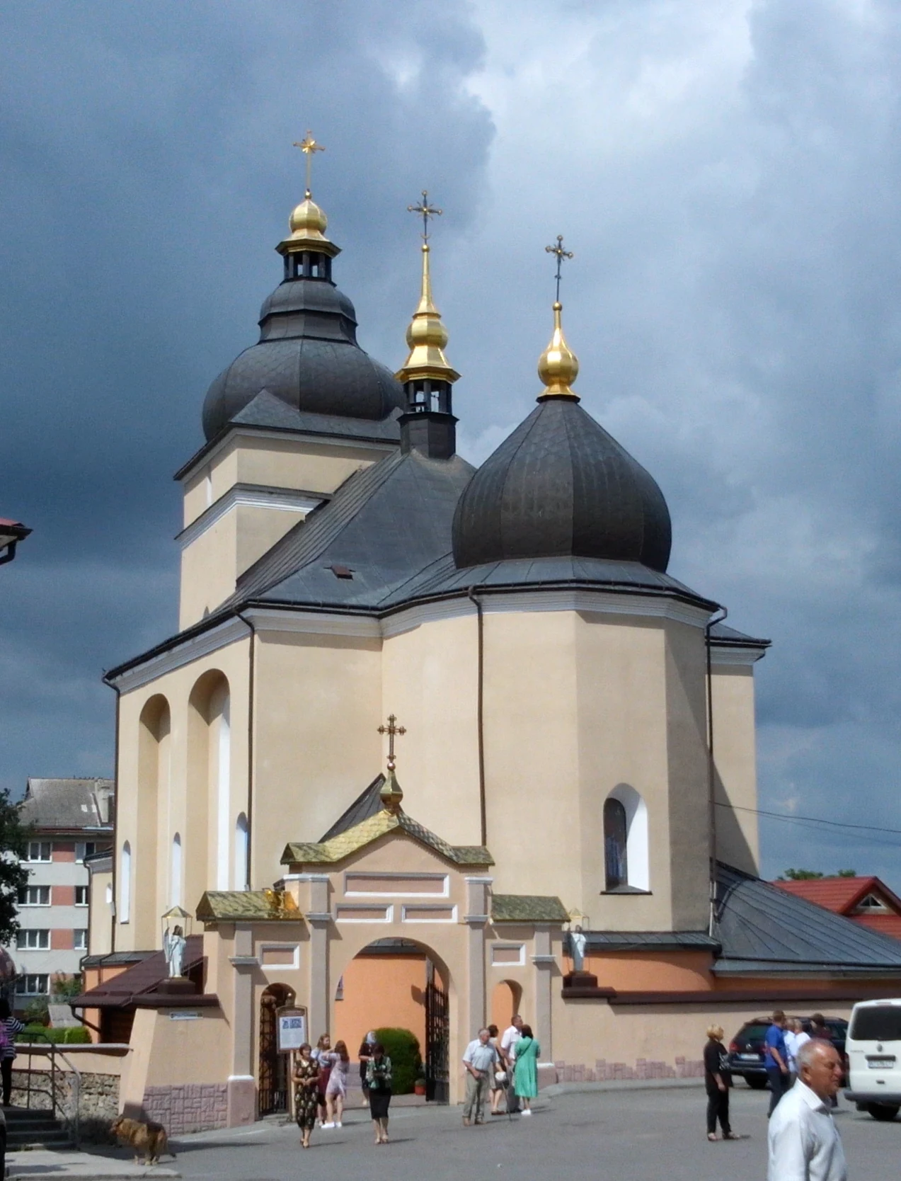 Світлі мури церкви Різдва Богородиці в Рогатині, висока башта й бані з хрестами за мурованою огорожею.